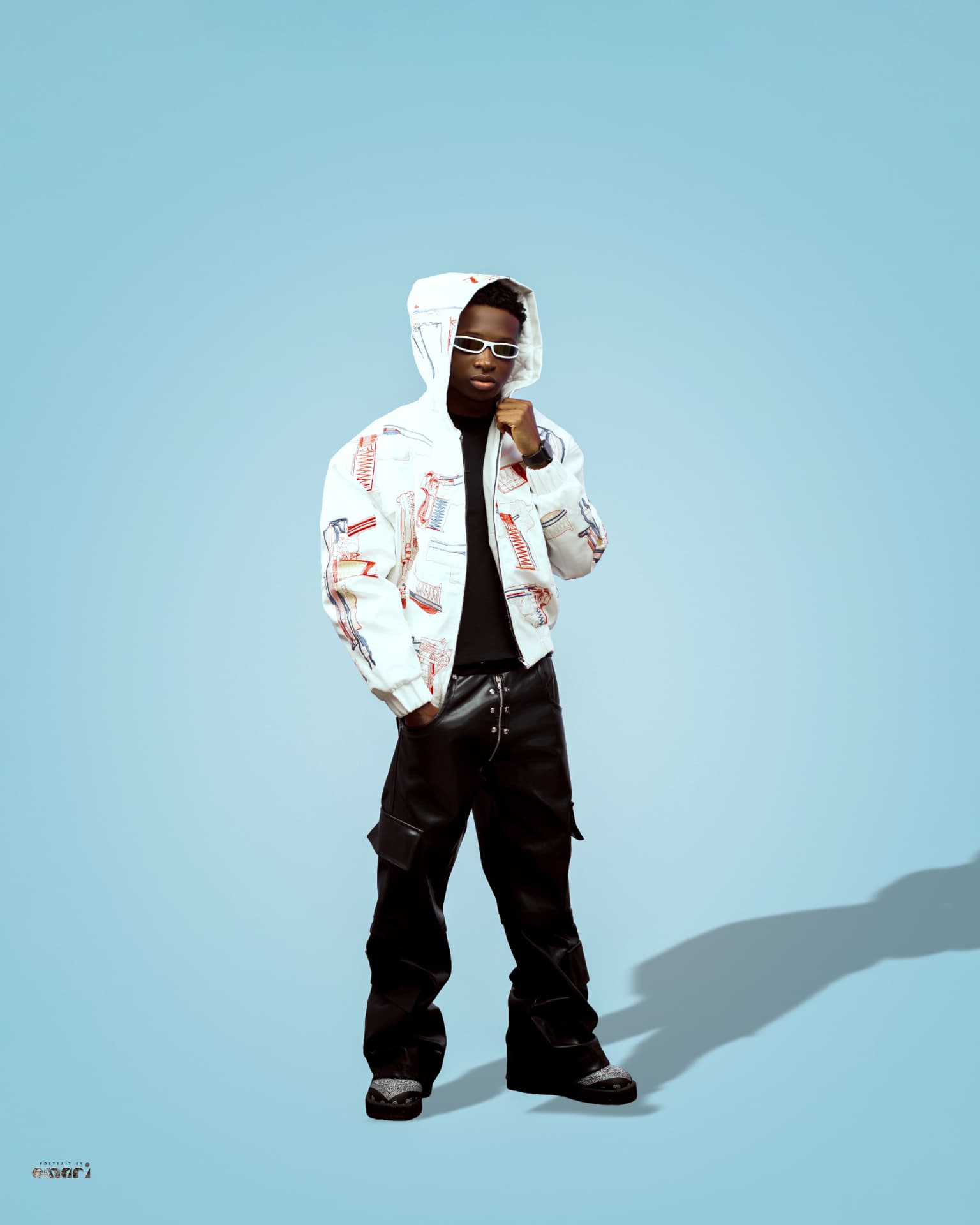 Boyyana in a white embroidered jacket and hood on a blue backdrop